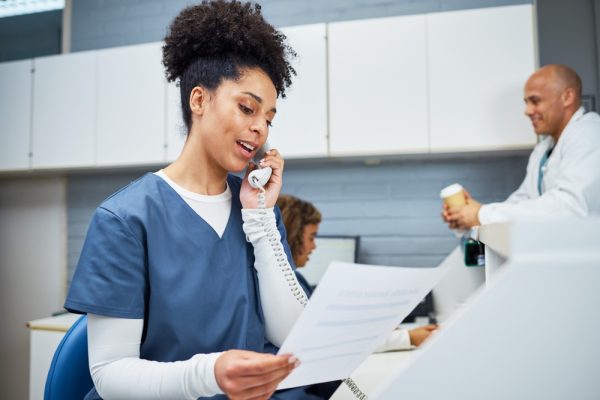 Woman on phone holding document, following up with patient for check-up.