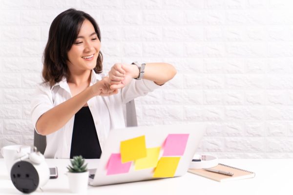 Virtual assistant looking on her watch, while sitting on table in office.