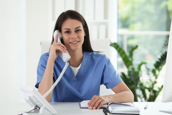 Virtual medical assistant working with clients by telephone at table in hospital office.