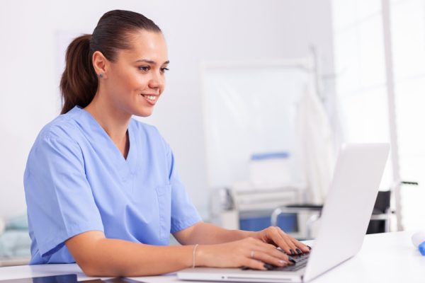 Virtual medical scribe positions with professionals using a laptop at a hospital office desk.
