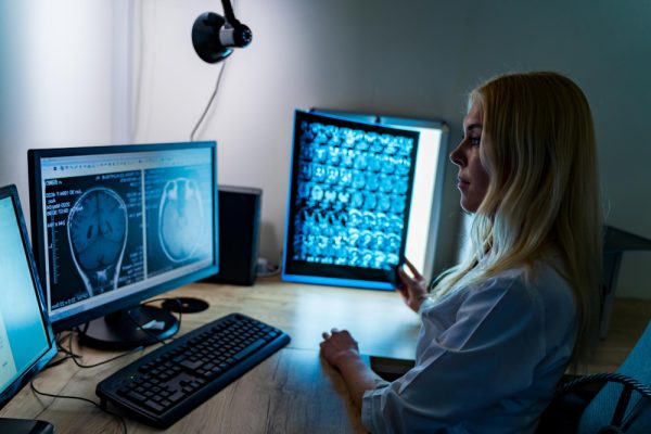 Woman reviewing brain X-ray on computer for neurology medical billing.