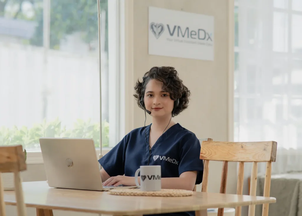 A person in a VMedX scrub top with a headset works on a laptop