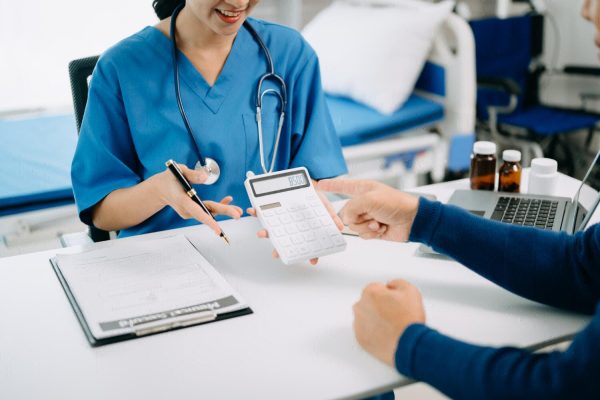 Medical billing assistant using calculator and tablet to manage medical costs at hospital.