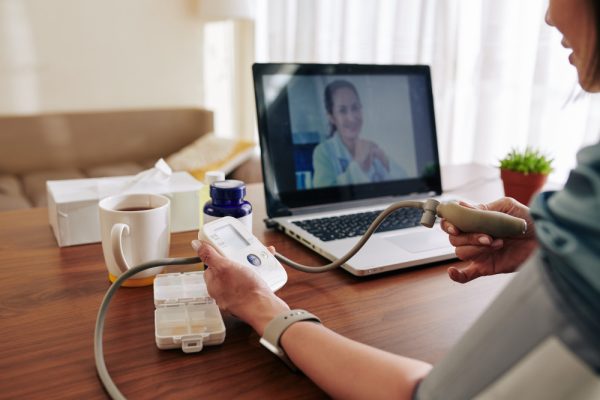 Woman measuring blood pressure at home using an electronic tonometer with guidance from a remote patient monitoring specialist.